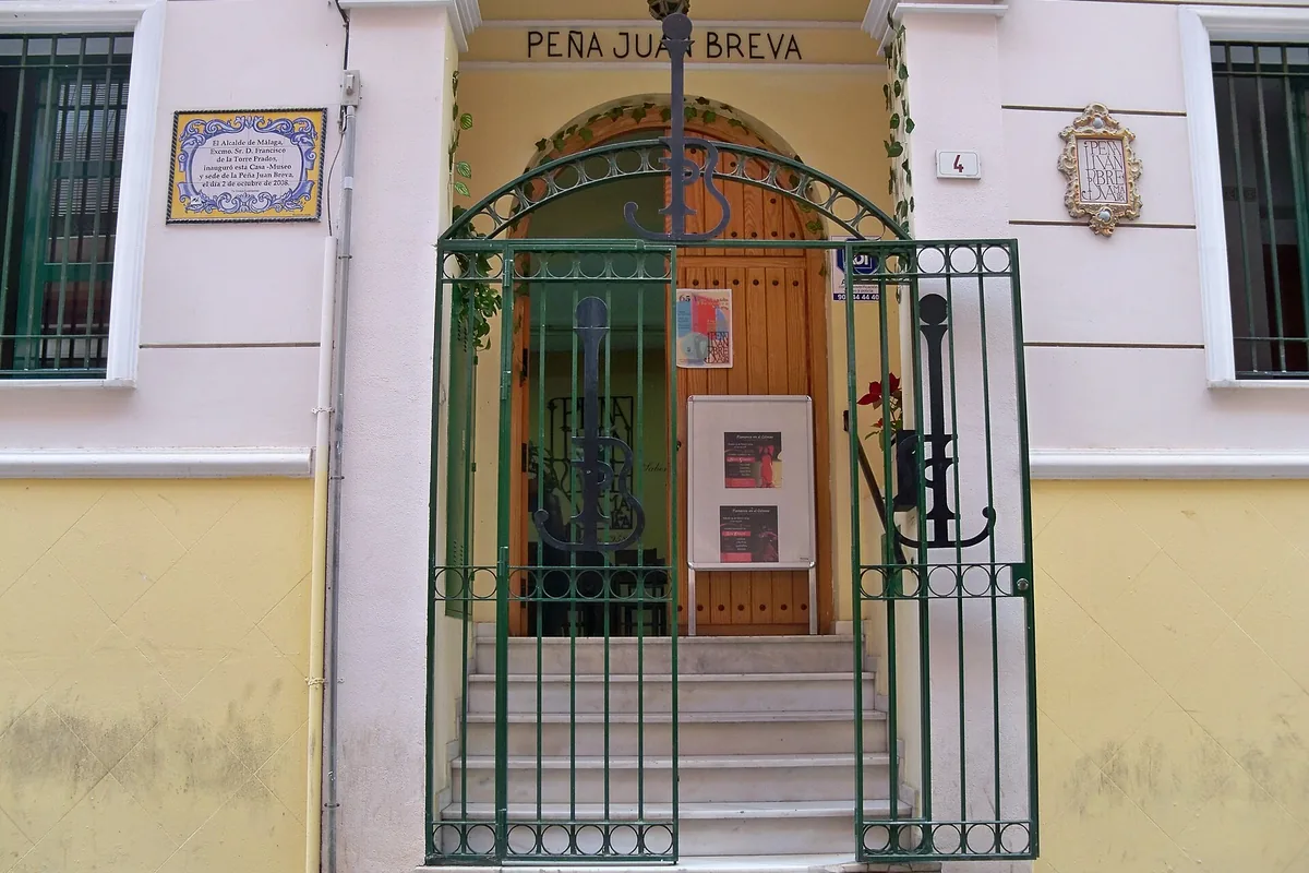 The green iron gate and arched wooden door of the Peña Juan Breva on a pink and yellow street front in Málaga